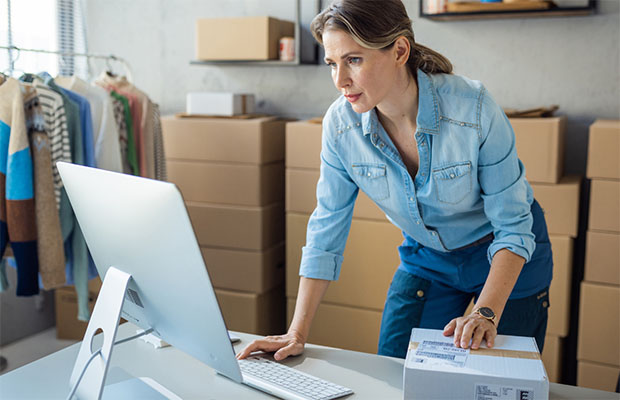 A woman standing in fron of a computer, in the process of shipping a packge.